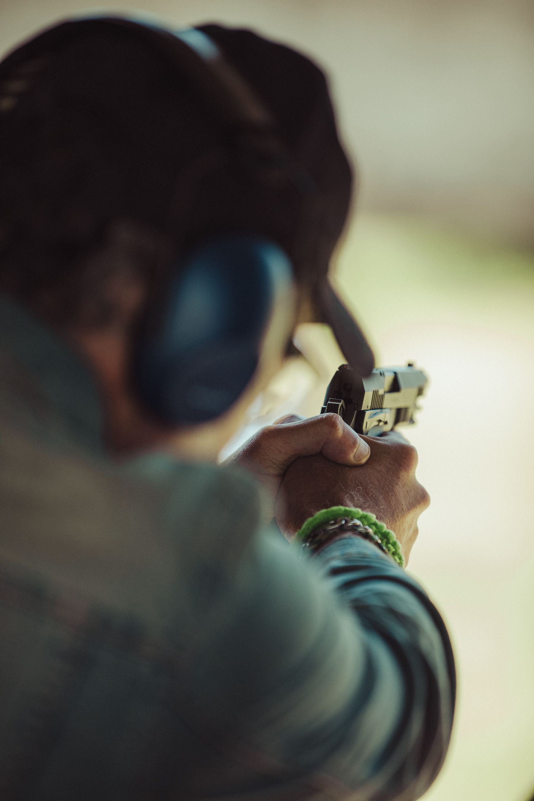 An individual aiming a pistol at a shooting range wearing ear protection.